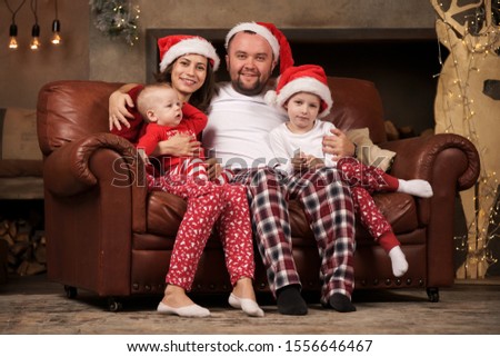 Picture of happy parents in Santa's caps and sons on leather sofa in studio