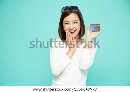 Happy Asian woman in white shirt holding credit card or cash advances isolated over light green background, Pay instead of money and specially curated benefits for lady card concept