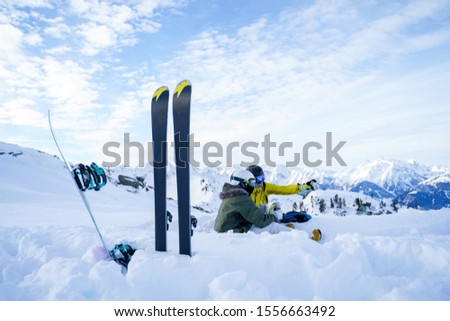 Picture of skis, ski poles against background of two sports women with thermos sitting in ski resort in winter.