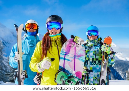 Picture of happy sports woman and men with skis and snowboard standing at ski resort