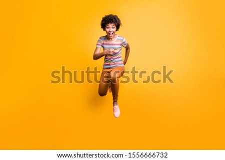 Full length body size photo of excited crazy approaching funny girl running towards you in search of sales in strpied t-shirt orange pants trousers footwear isolated vivid color background yellow