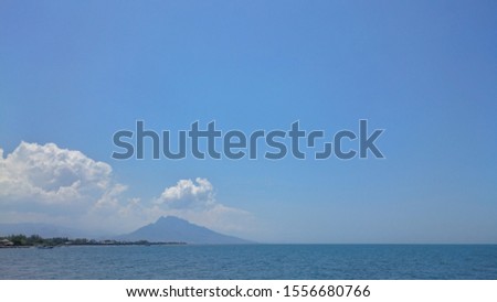 The cloudy sky with gradient blue color, cloudy, mountain and calm ocean at the bottom of the photo