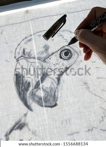 Drawing a parrot with gel pen on back lit fabric. Close up of technique to copy outline of an image onto fabric using a light box, for crafts such as collage quilting. Vertical.
