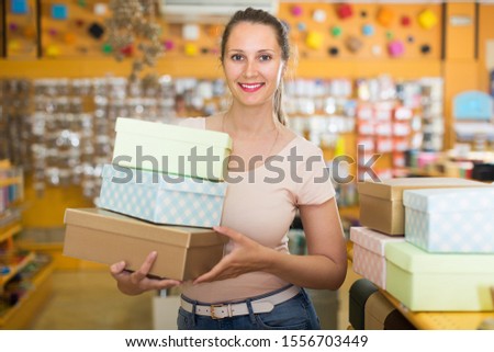 Cheerful girl with gift boxes in her hands chooses accessories for gift in store