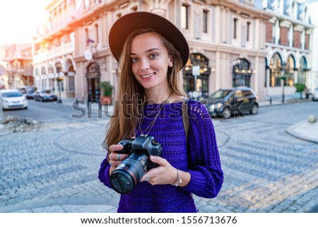 Happy beautiful casual stylish fashionable traveler woman photographer in hat holding dslr camera taking pictures while walking around european city