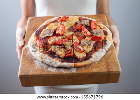 Woman's hands holds homemade pizza with tomato, bacon, salami and cheese. Wooden cutting board.