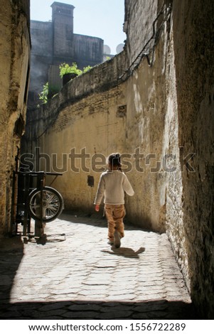 An unidentified young girl with her hair in a braid walking down a narrow alleyway in the Medina of Fez, Morocco on a sunny day with contrasting shadows.  Image has copy space.