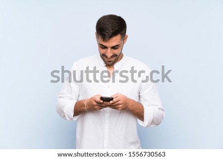 Handsome man with beard over isolated blue background sending a message with the mobile