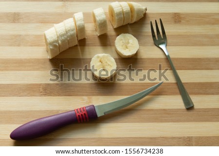 cut banana with kitchen knife and dessert fork cutlery objects in wooden striped background textured surface 