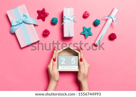 Top view of female hands holding calendar on pink background. The twenty fifth of December. Holiday decorations. Christmas time concept.