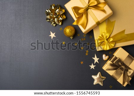 Top view of golden gift boxes with shiny satin bows and glittering christmas tree toys as attributes of party on black chalk board background with copy space