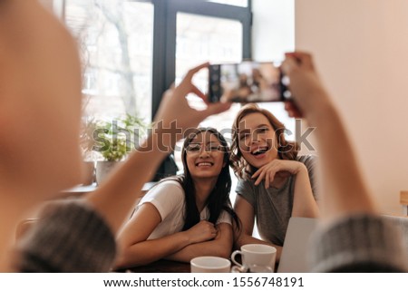 Cropped view of girl with smartphone and her laughing friends. Selective focus of photofrapher taking picture of happy women.