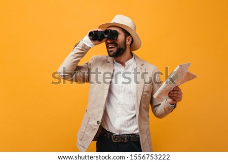 Man in hat looks into binoculars and holds map on orange background