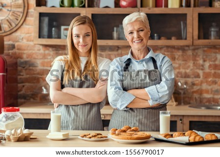 Adult mother and daughter baking together at home, posing with homemade pastry with arms crossed