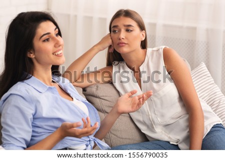 Jealous Woman Listening With Envy To Her Friend Bragging About Great Life Sitting On Sofa Indoor. Selective Focus Royalty-Free Stock Photo #1556790035