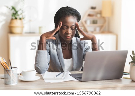 Brainstorm. Overworked african american businesswoman touching temple, trying to concentrate while sitting at workplace in modern office