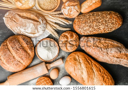 Fresh bakery food, rustic crusty loaves of bread and buns on black stone background. Top view and copy space for text.