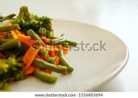 Healthy, natural food. Vegetables: carrots, broccoli, steamed asparagus, lie on a white bowl. Close-up. Blur Shallow depth of field. Out of focus. Side view.