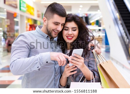 Consumerism concept. Spouses using smartphone, searching sales online, walking in mall