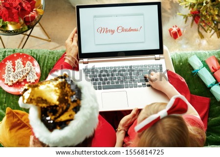 Upper view of modern mother and child sitting on sofa in the modern living room at Christmas writing Merry Christmas email on a laptop.