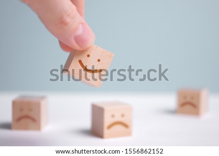 A man holds a wooden cube with a picture of a positive face on the background of negative emotions. Close up. Royalty-Free Stock Photo #1556862152