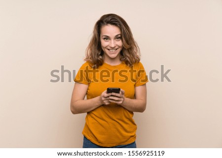 Young blonde girl over isolated background sending a message with the mobile