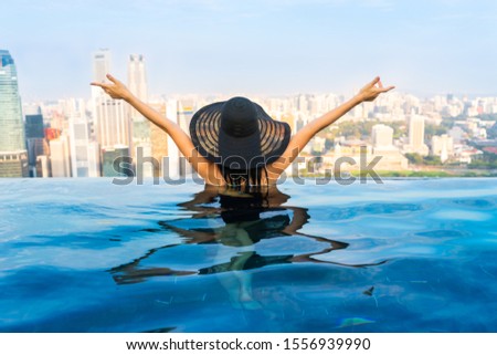 Young woman in a roof top swimming pool, infinity pool with beautiful city view. Vacation in Singapore.