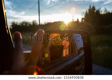 Photographer self portrait taken with a DSLR from the passengers seat of a SUV. Lens flares and sunset are seen in the background. 