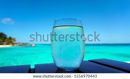 Clear glass water cocktail with blue turquoise ocean island background