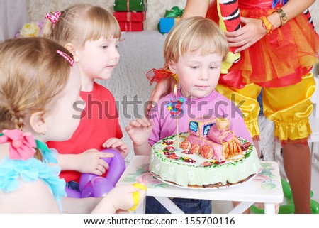 Three kids look at birthday cake with locomotive at funny children party. Focus on girl and boy on right.