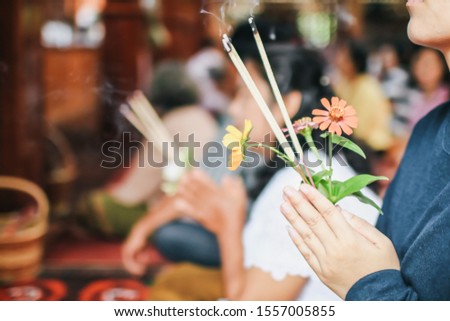 An asian woman keep a lotus, candles and incense sticks in hands for praying respect to the buddha statue on New year