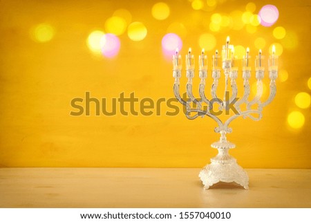 Religion image of jewish holiday Hanukkah with menorah (traditional candelabra) and oil candles over yellow background