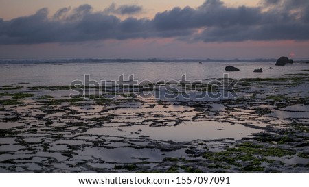 Seascape. Dramatic sunset at the beach. Ocean low tide. Horizon line. Sky with clouds. Colorful landscape. Blue sunlight. Water reflection. Horizontal background banner. Nyang Nyang beach, Bali.