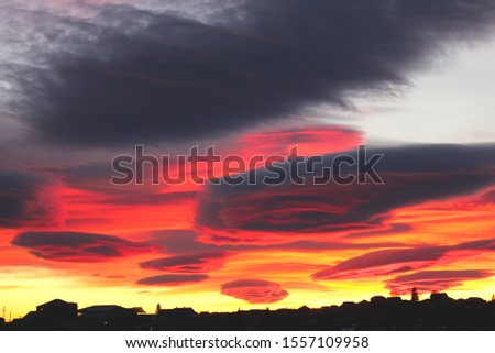 Beautiful sunset with red ribbon clouds like roses. Red-blue sunset over the city with dark clouds. Dark silhouette of the city with a beautiful dawn. Artistically blurry.