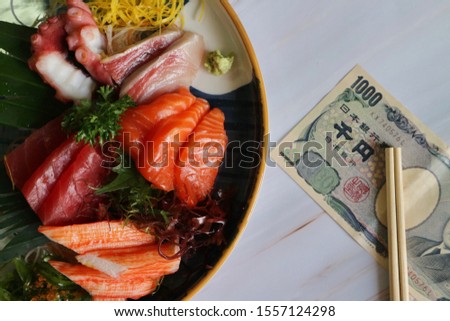 Fresh salmon, tuna, scallops with green leaf, seaweed and wasabi on plate with wood chopsticks, money on marble pattern table
