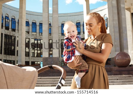 Fashionable modern mother on a urban street with a pram. Young mother walks with a child in the city. Beautiful young woman with a child in a baby carriage