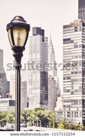 Retro toned picture of a street lamp with New York City blurred skyline in background, USA.