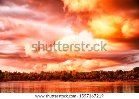 Sky with fantastic, amazing, stormy, disturbing red clouds over the river on a summer or autumn evening. Dramatic landscape with sky full of cloud at sunset