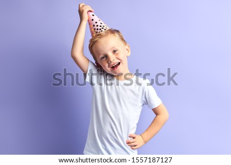Portrait of happy little boy wearing birthday cap on head, isolated over purple background