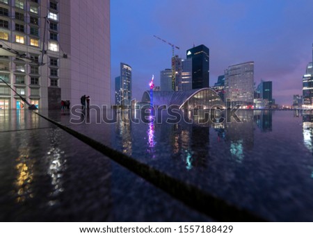 La Défense modern suburb of Paris with colorful Architecture reflected by wet floor at blue hour late Night. Grand Arche panorama on a rainy november evening illuminated facades of tall buildings.