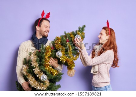 Time for winter holidays, young lovely couple cheerfully spending time at home, decorating Christmas tree, isolated photo on violet background, happy Christmas moments