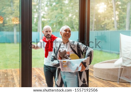 Cheerful positive couple un casual clothes holding boxes snter new house. Buying new house with big window view on garden Royalty-Free Stock Photo #1557192506