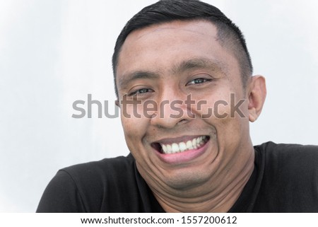 A closeup face of an Indonesian Asian man with an awkward smile showing his teeth on balck t-shirt and white background. He has double and triple chins Royalty-Free Stock Photo #1557200612