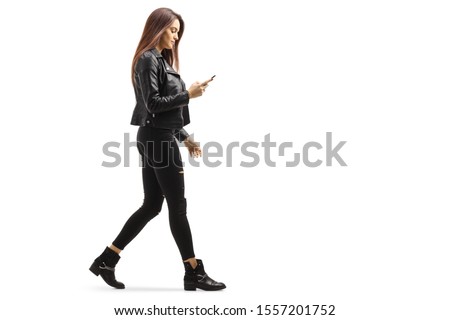 Full length profile shot of a young female walking and looking at her mobile phone isolated on white background Royalty-Free Stock Photo #1557201752