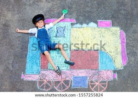 Happy little kid boy having fun with train or steam locomotive picture drawing with colorful chalks on ground. Children, lifestyle, concept. funny child playing and dreaming of future and profession