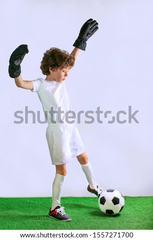 Kids - soccer champion. Boy goalkeeper with a surprised face in football sportswear with ball on gray background. Sport concept.Copy space.