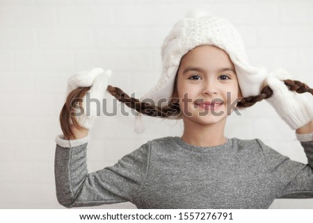 Happy laughing child girl in a winter white knitted hat and mittens on light background