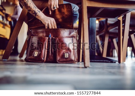 Cropped picture of businessman taking out tablet of his bag. Cafeteria interior.