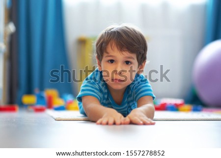 Sad face of Toddler boy lying down on wooden floor at playroom