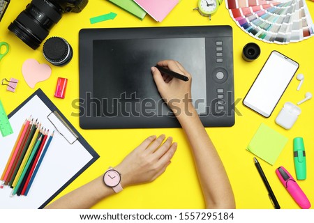 Professional designer drawing with graphic tablet at yellow table, top view